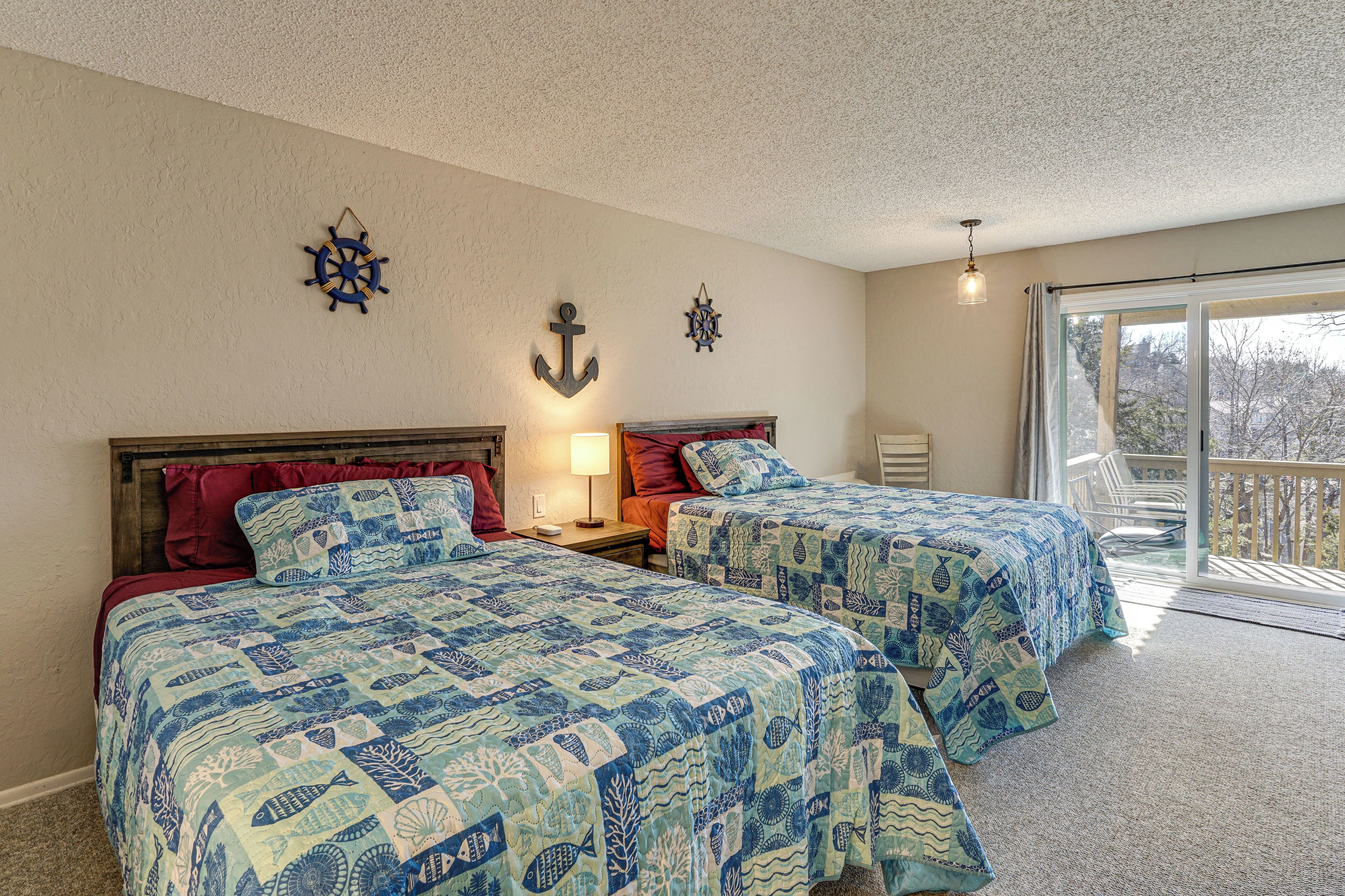 A bedroom with two beds, nautical-themed bedding, a large window with a view, and a sliding glass door to a balcony.