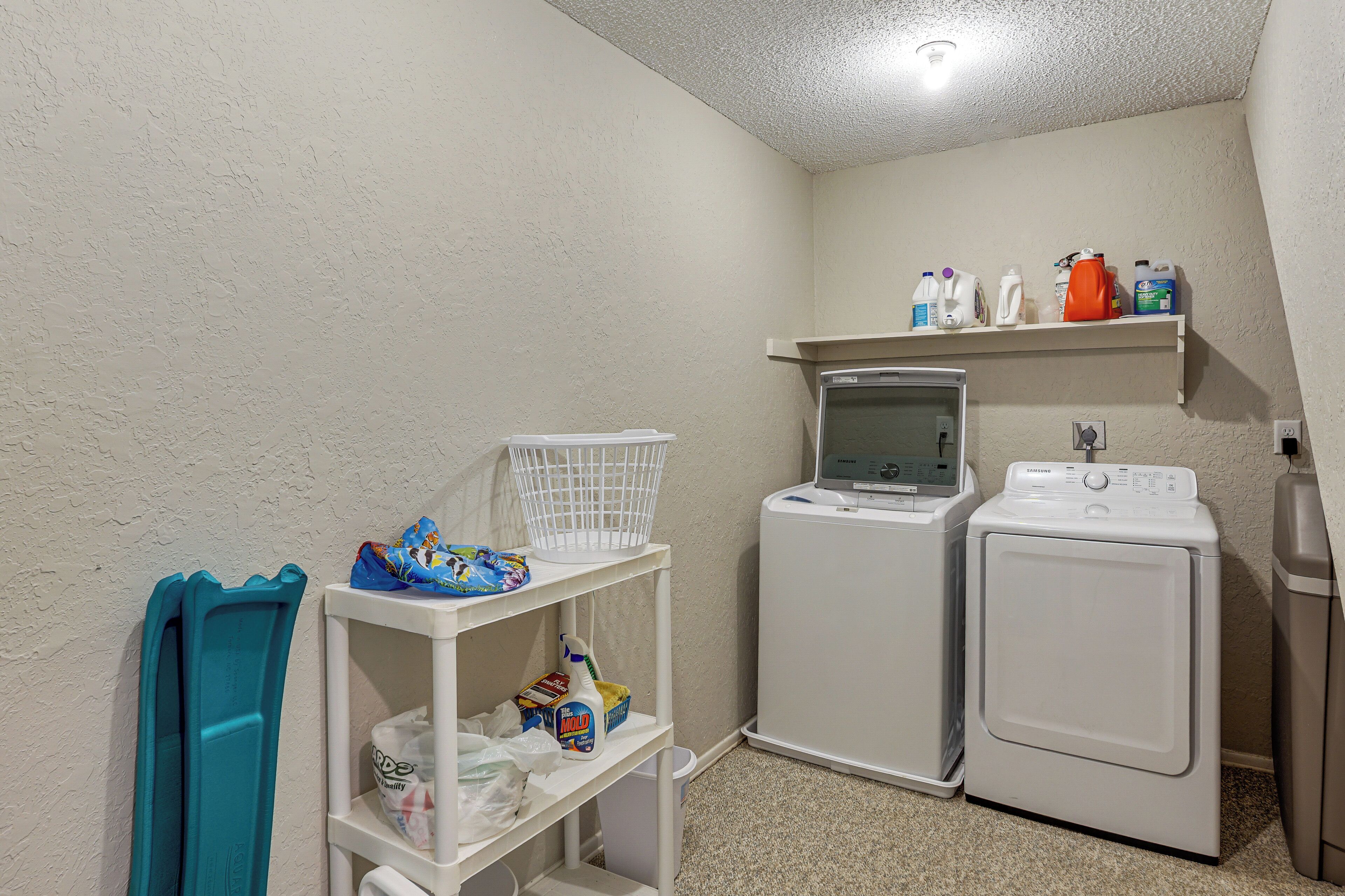 A laundry area with a washing machine, dryer, and shelves with cleaning supplies.
