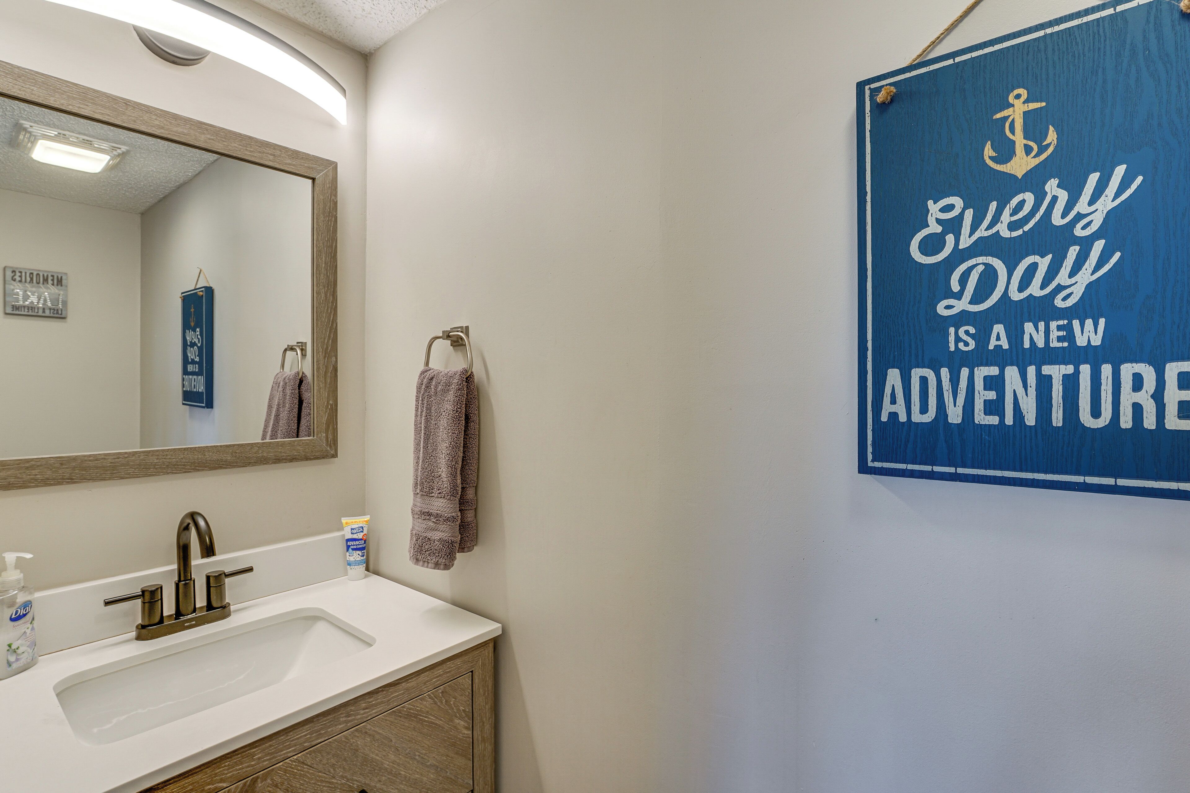 A bathroom with a sink, mirror, and a motivational sign that reads "Every Day is a New Adventure".