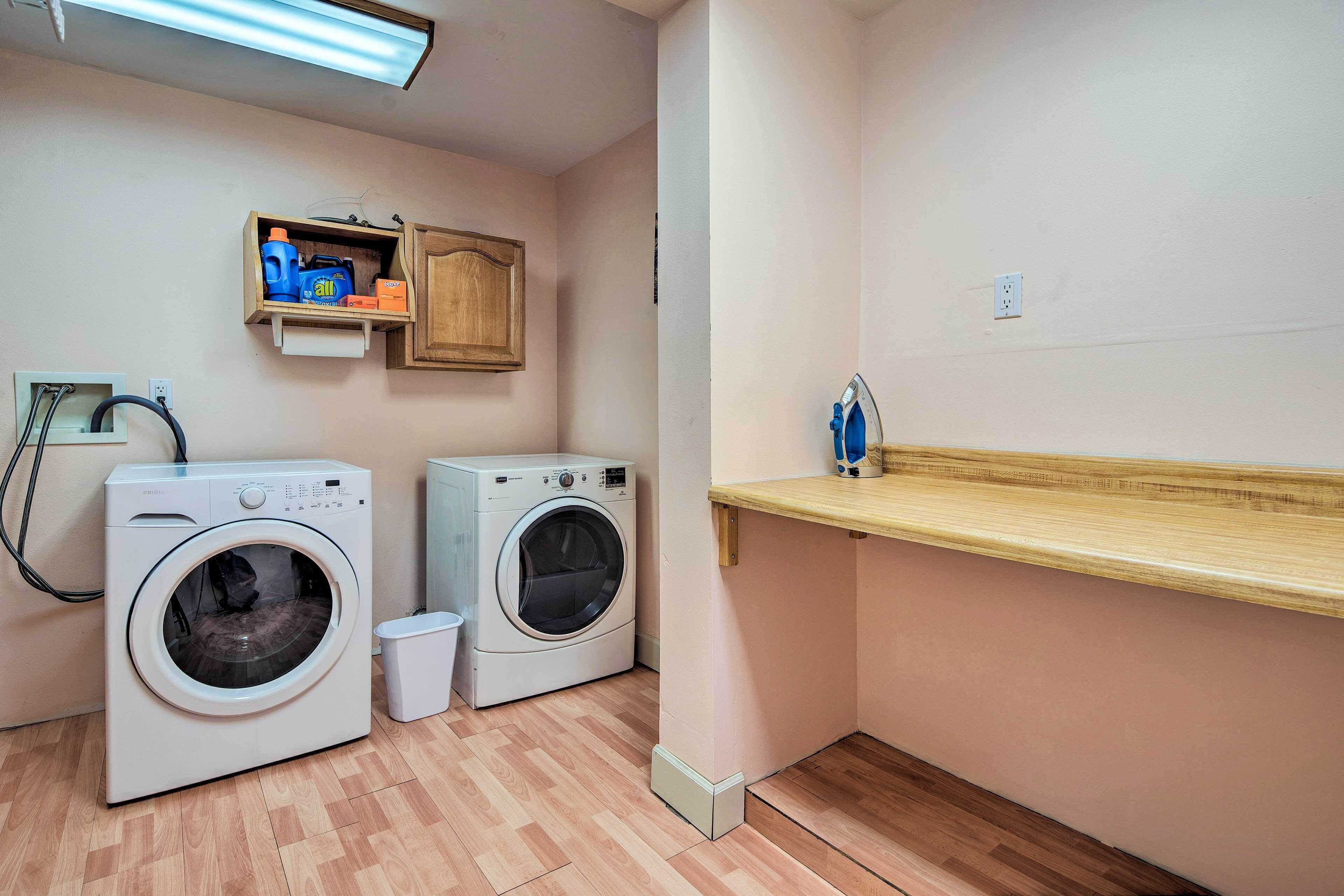 A laundry room with two front-loading washing machines, a wooden shelf with laundry supplies, and a small cabinet above the machines.