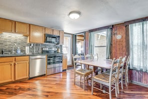 A kitchen with wooden cabinets, a dishwasher, a microwave, and a dining area with a table and chairs. - Killington Area Escape w/ Deck, Views & Hot Tub! (Stockbridge)