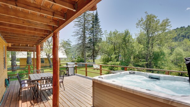 En træterrasse med jacuzzi, udendørs møbler og udsigt til en skovklædt skråning.