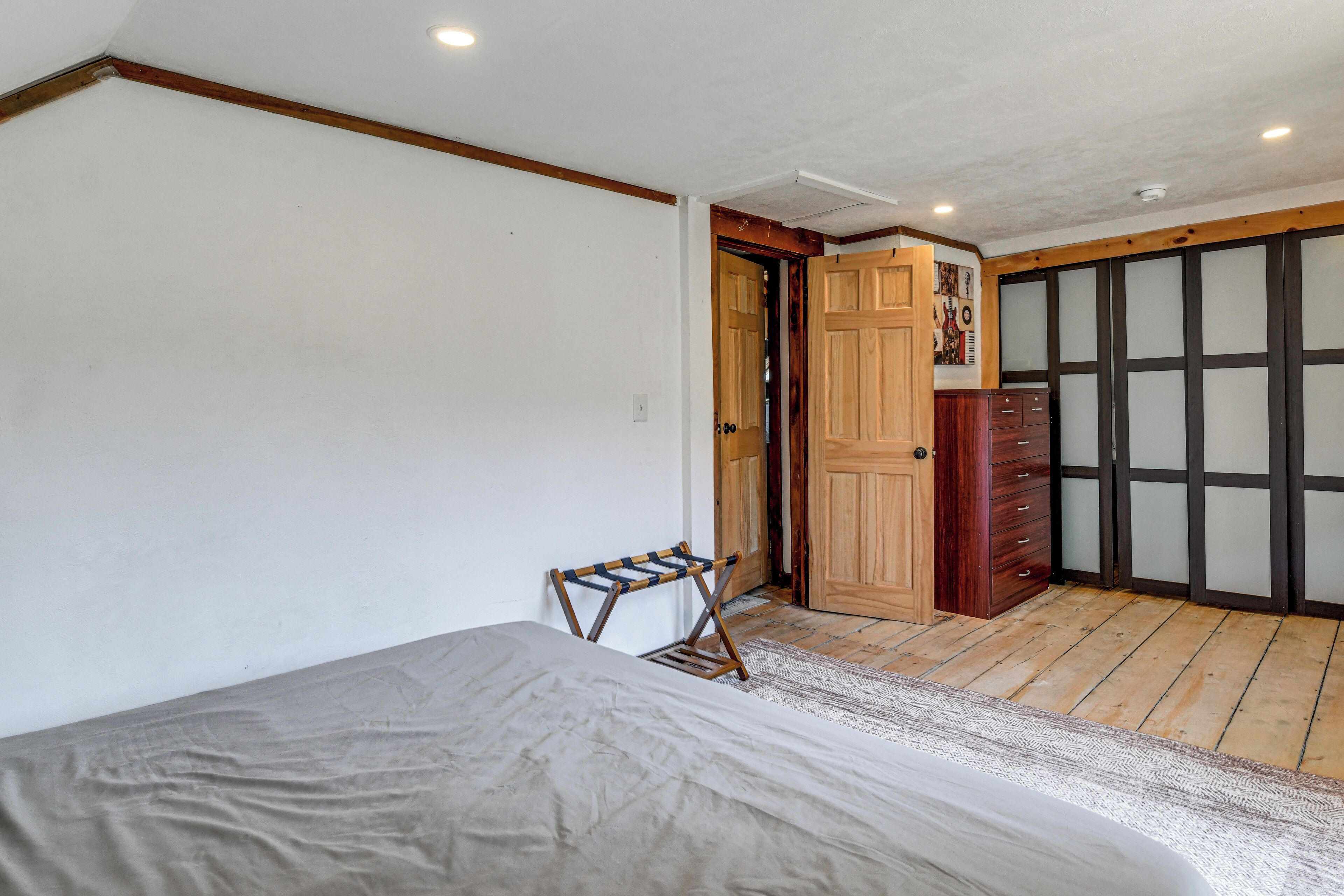 Un dormitorio con una cama, una puerta de madera, un armario y una silla plegable pequeña.