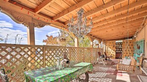 Un espacio al aire libre techado, con techo de madera, una mesa con mantel colorido, un sillón colgante y una lámpara decorativa.