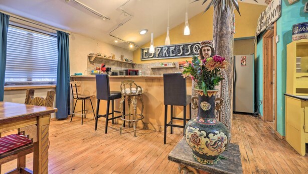 Un interior acogedor con una mesa de comedor de madera, taburetes de bar, un jarrón decorativo y un letrero que dice "ESPRESSO".