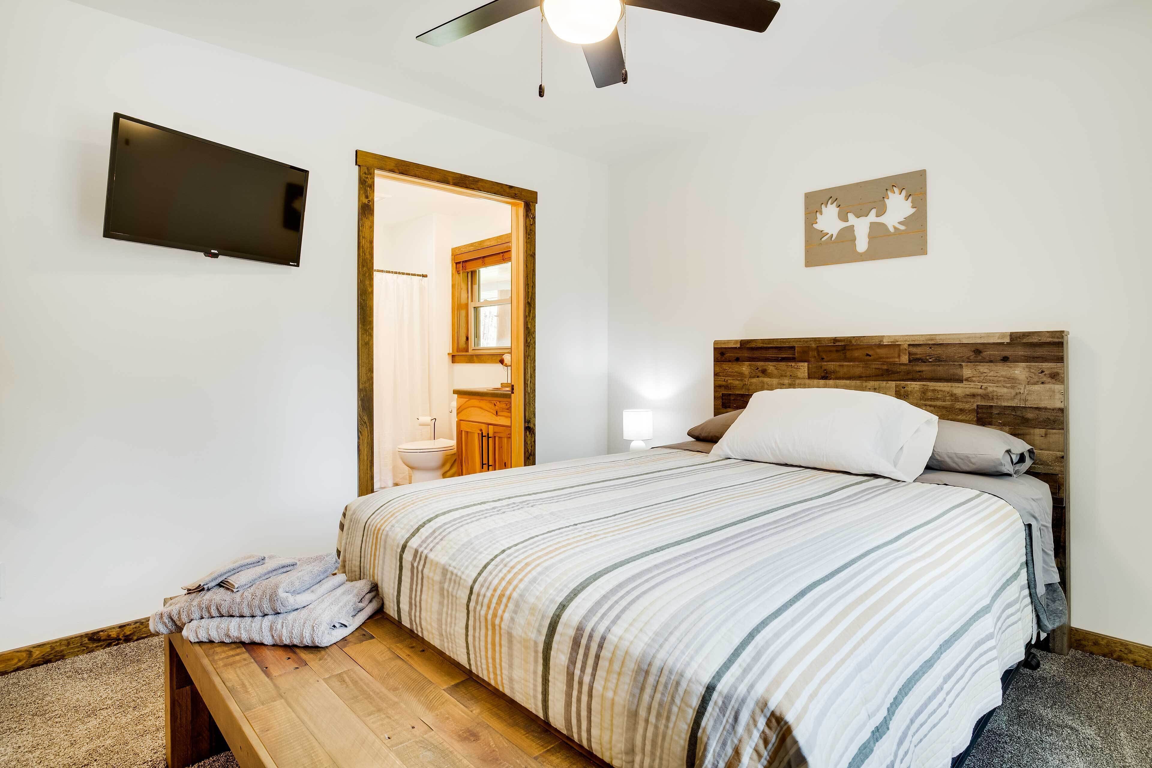 A bedroom with a bed, a wooden bench, a ceiling fan, a flat-screen TV, and a wooden headboard.
