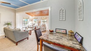 A spacious living room with a large window, a dining area with a marble table, and a cozy seating area with a sofa and chairs. - Historic Cabin w/ Yard: 1 Mi to Lake Spavinaw! (Spavinaw)