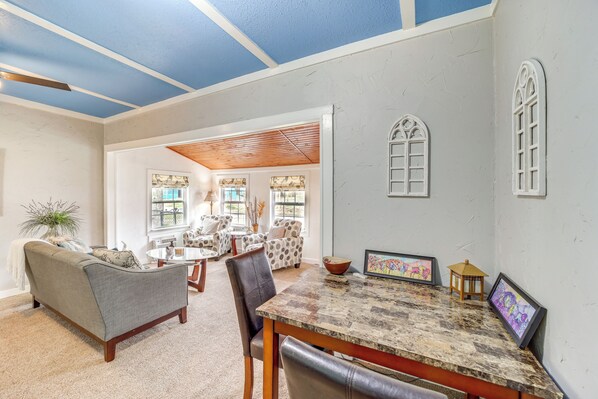 A spacious living room with a large window, a dining area with a marble table, and a cozy seating area with a sofa and chairs. - Historic Cabin w/ Yard: 1 Mi to Lake Spavinaw! (Spavinaw)