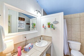 A bathroom with a white sink, mirror, and toilet, with a window and a shower curtain. - Historic Cabin w/ Yard: 1 Mi to Lake Spavinaw! (Spavinaw)