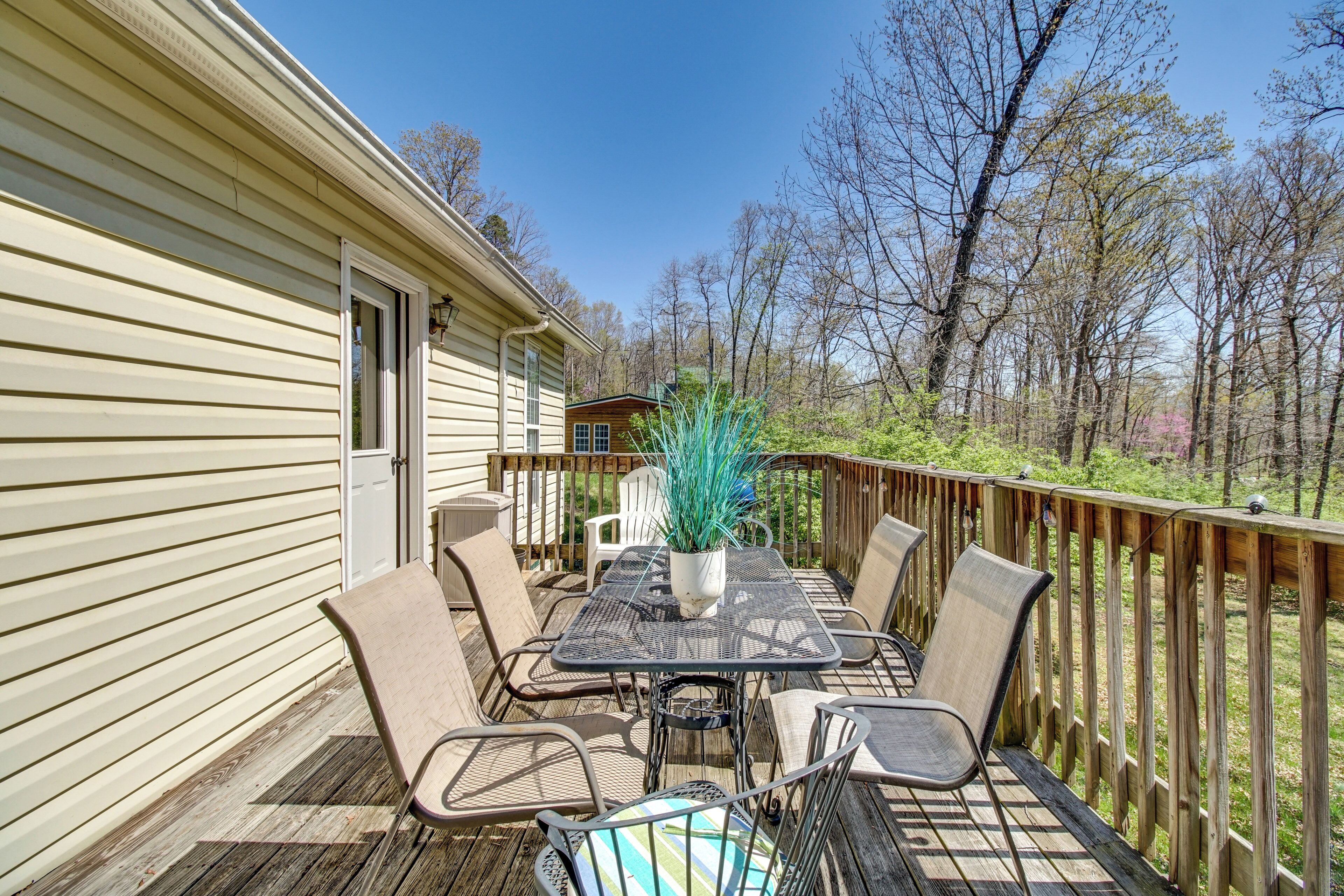 A deck with a table and chairs, a potted plant, and a view of a forested area.