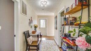 Un couloir avec un banc en bois, un tapis blanc et une bibliothèque remplie de livres et de jeux de société.