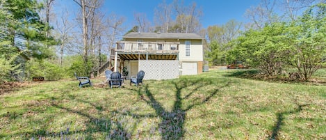 A house with a covered patio, a lawn with purple flowers, and trees in the background.