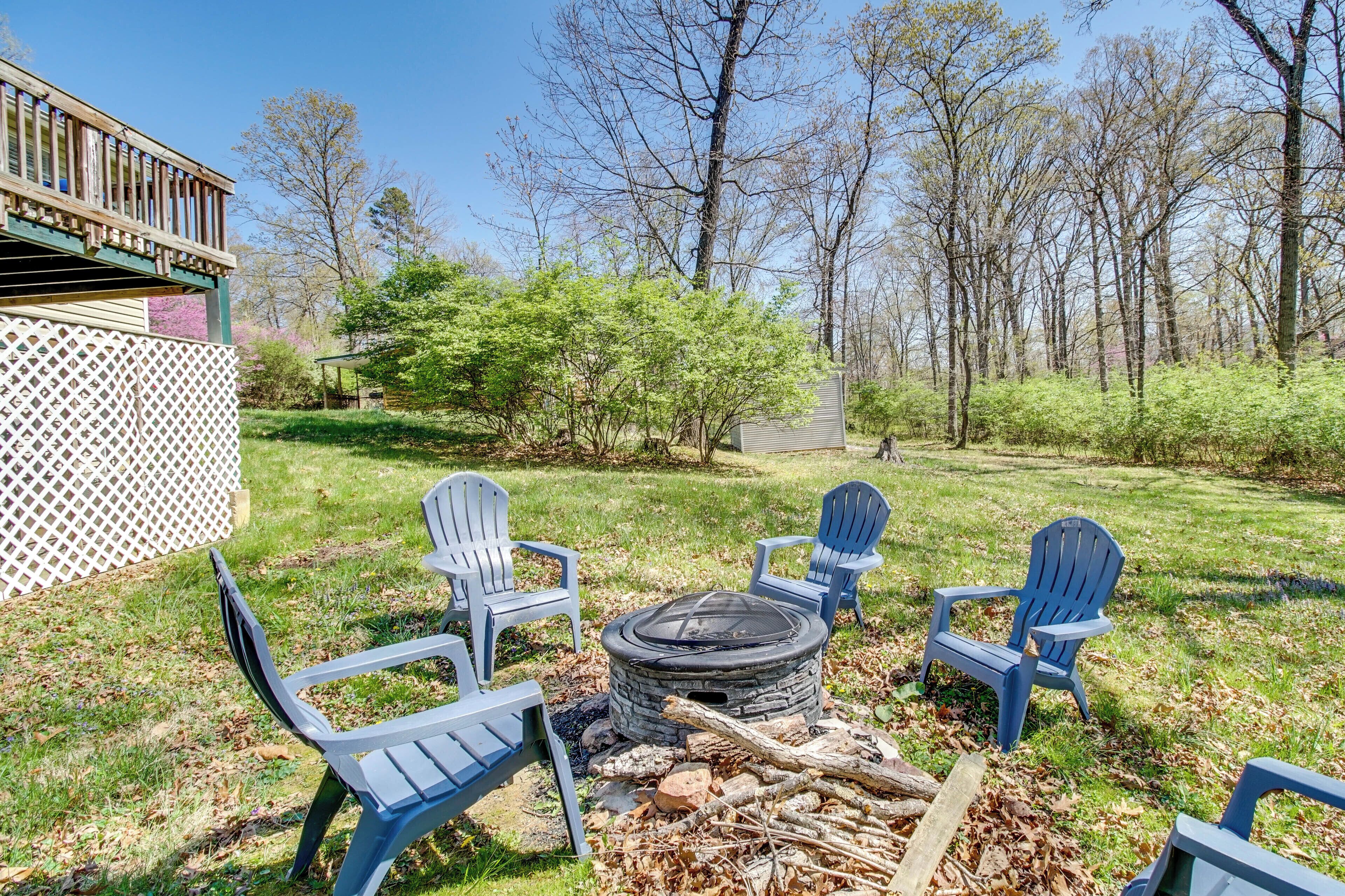 A backyard with a fire pit, four Adirondack chairs, and a wooden deck.