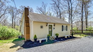 Une petite cabane à un seul étage, dotée d’une cheminée, d’une porte d’entrée et d’un petit porche agrémenté de plantes en pot et d’un banc.