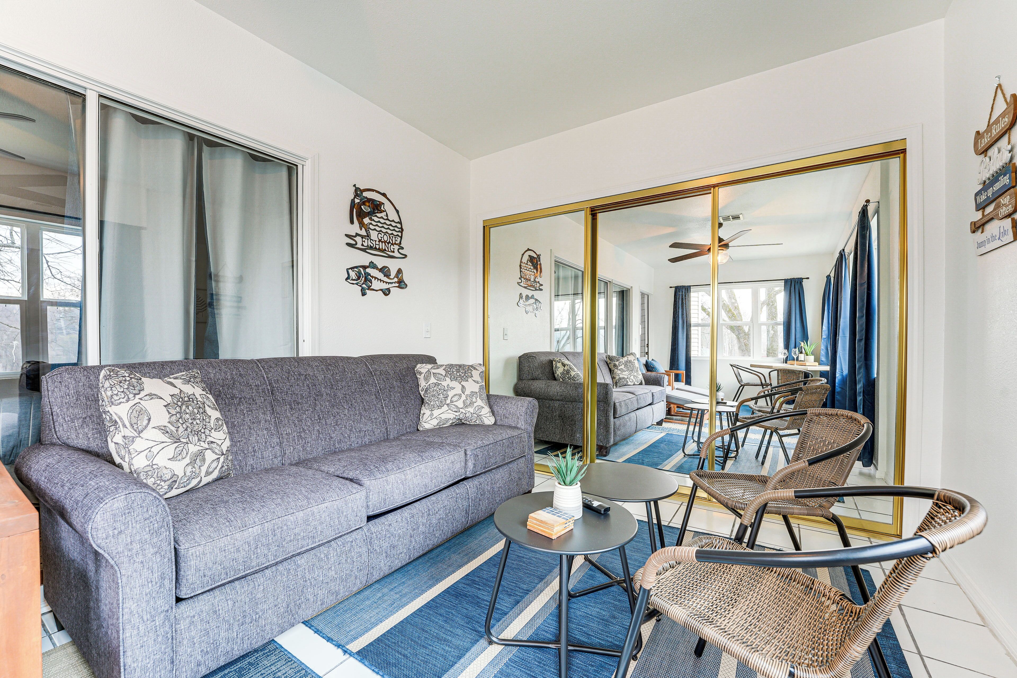 Un salon moderne avec un canapé gris, une petite table ronde, des chaises en osier et un grand miroir qui reflète la pièce.