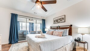 A bedroom with a large bed, a ceiling fan, a nightstand with a lamp, and a view of the outdoors through a sliding door. - Sunroom, Fireplace: Lakefront Branson Condo (Branson)
