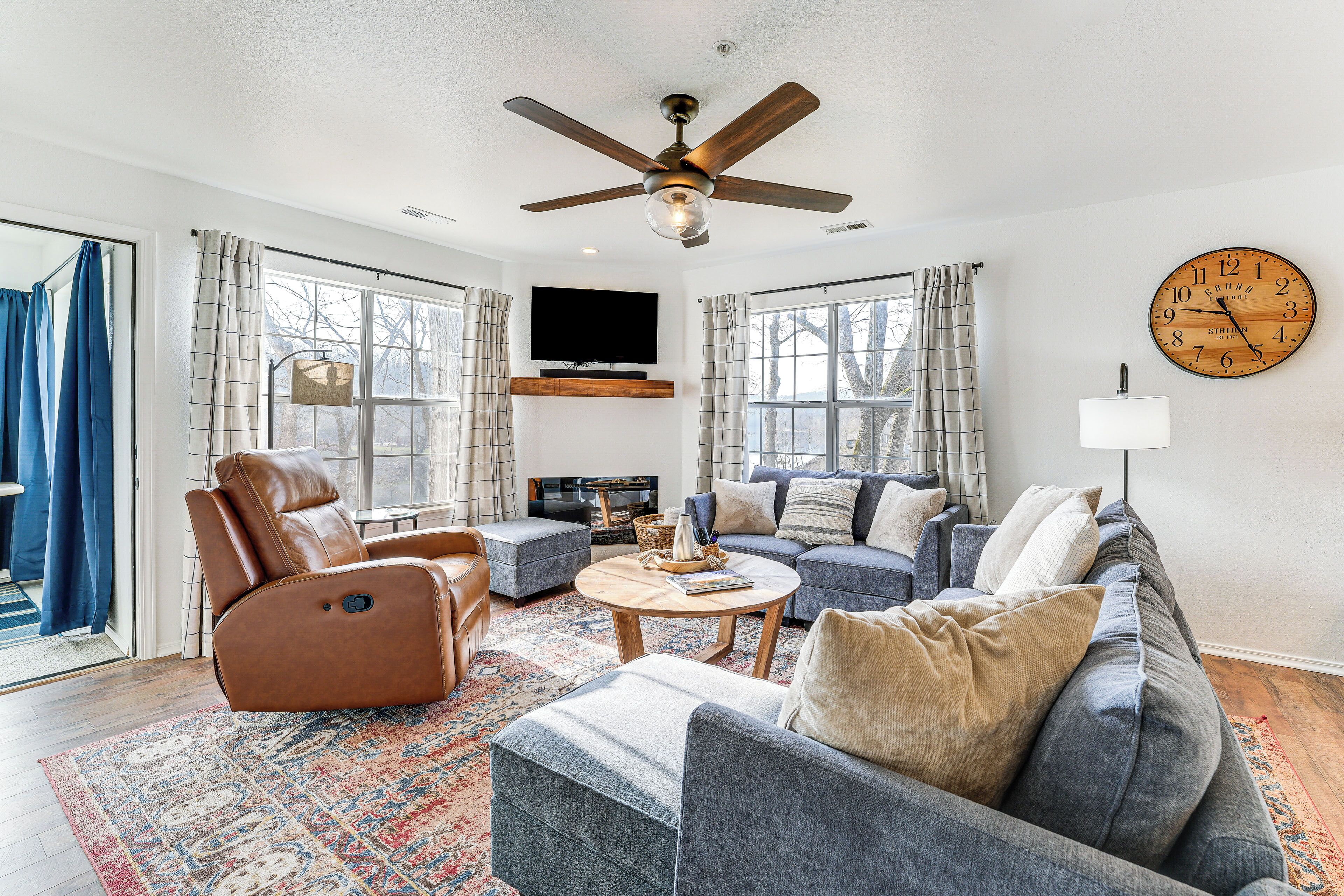 A living room with a ceiling fan, a large clock, a sofa, a coffee table, and a television.