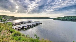 A waterfront dock area with multiple piers extending into calm water, surrounded by lush greenery and hills in the background. - Clifftop Kaiser Condo for Shootout Weekend Groups (Kaiser)