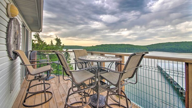 A wooden deck with outdoor furniture, a round table, and chairs, overlooking a body of water and a forested landscape. - Clifftop Kaiser Condo for Shootout Weekend Groups (Kaiser)