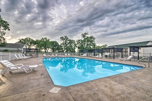 Piscina com espreguiçadeiras e área coberta, cercada por árvores e um céu nublado.