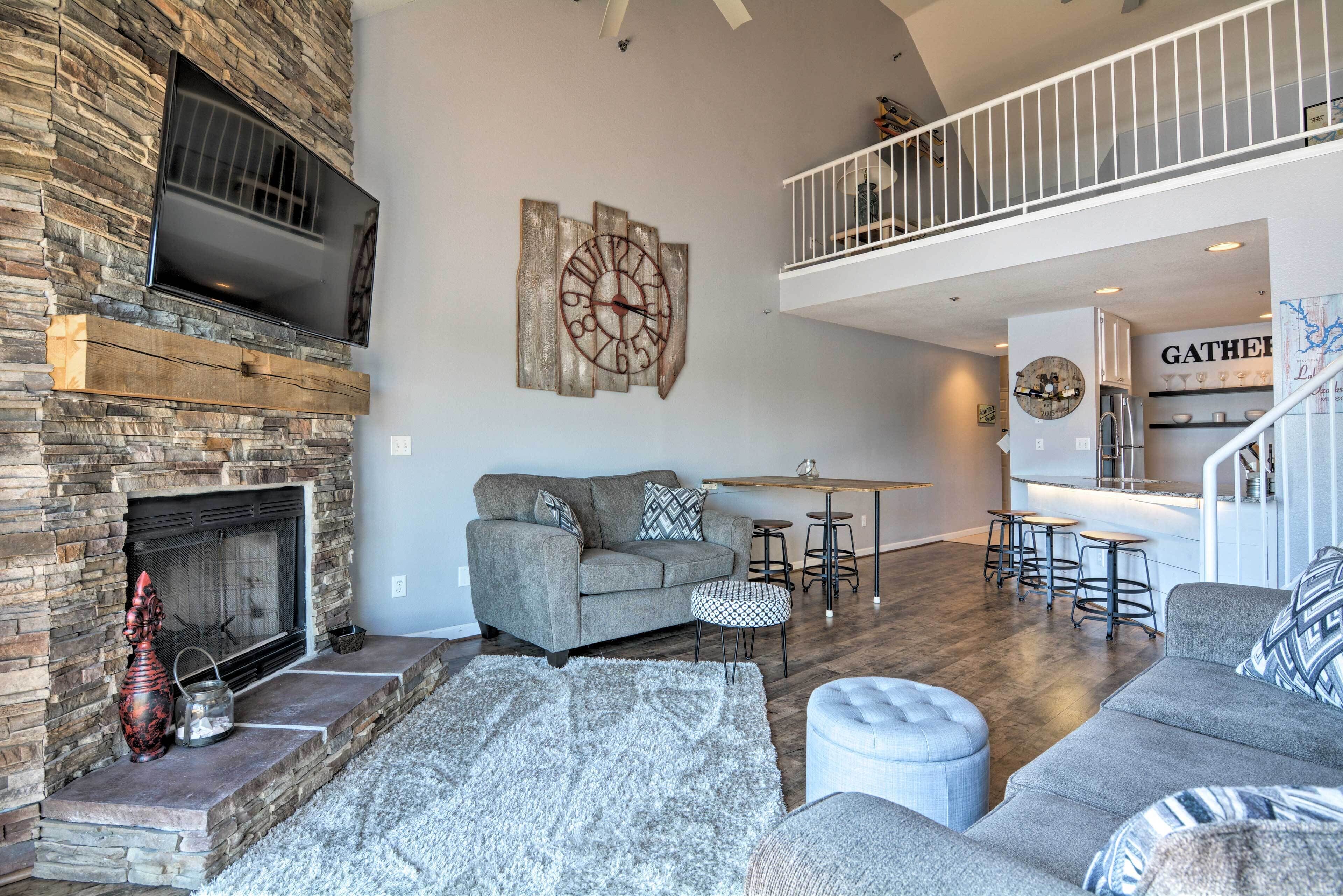 A spacious living area with a fireplace, a grey sofa, a coffee table, and a staircase leading to an upper level.