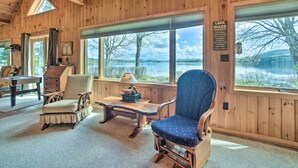 A wooden cabin interior with a pool table, two chairs, a lamp, and a view of a lake. - Waterfront Lake Pleasant Getaway w/ Kayaks, Grill! (Lake Pleasant)