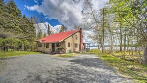 A wooden cabin with a red roof, a chimney, and a porch, surrounded by trees and a gravel driveway. - Waterfront Lake Pleasant Getaway w/ Kayaks, Grill! (Lake Pleasant)
