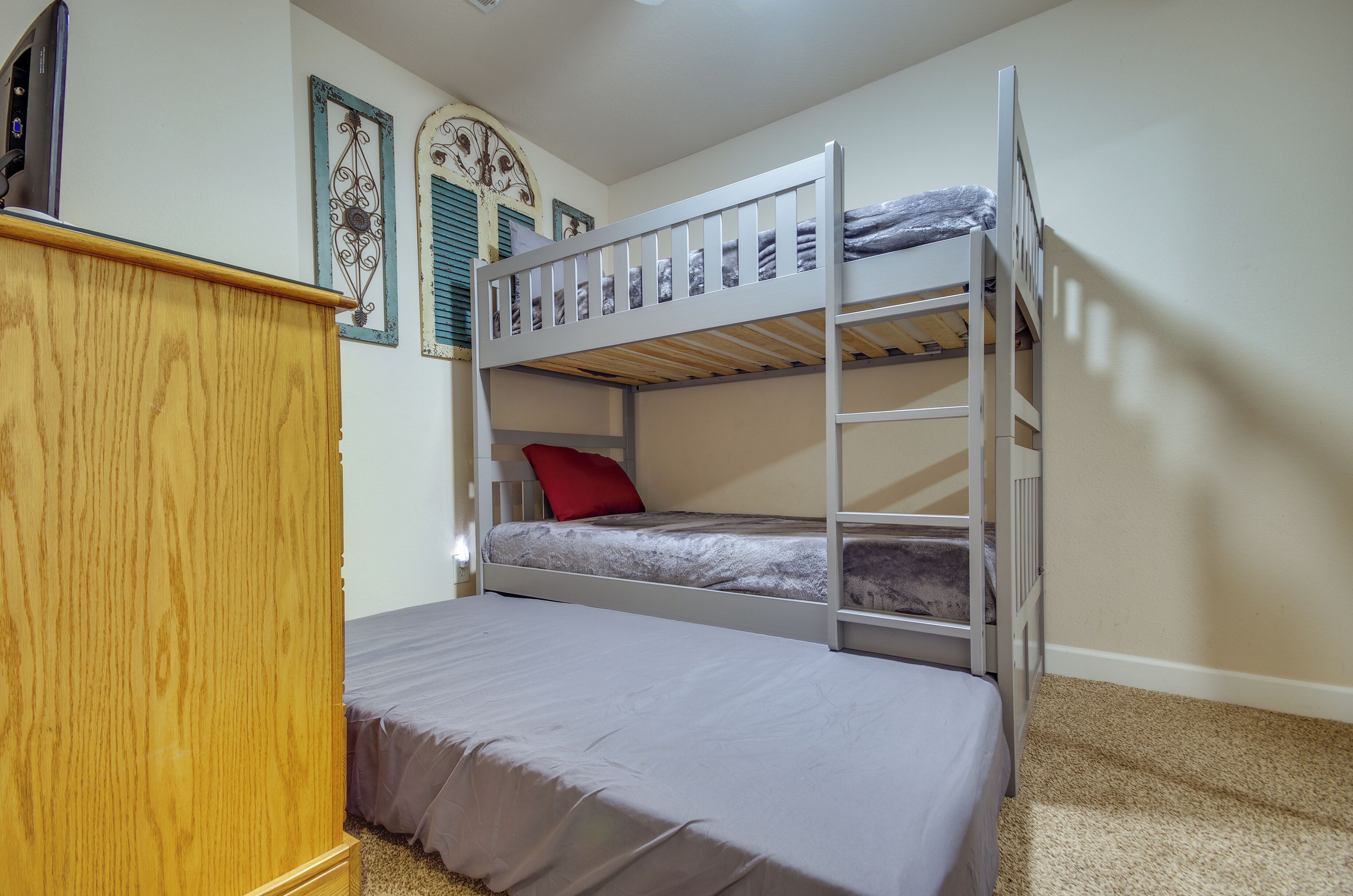 A bunk bed with a lower bunk, a wooden dresser, and a wall with decorative elements.