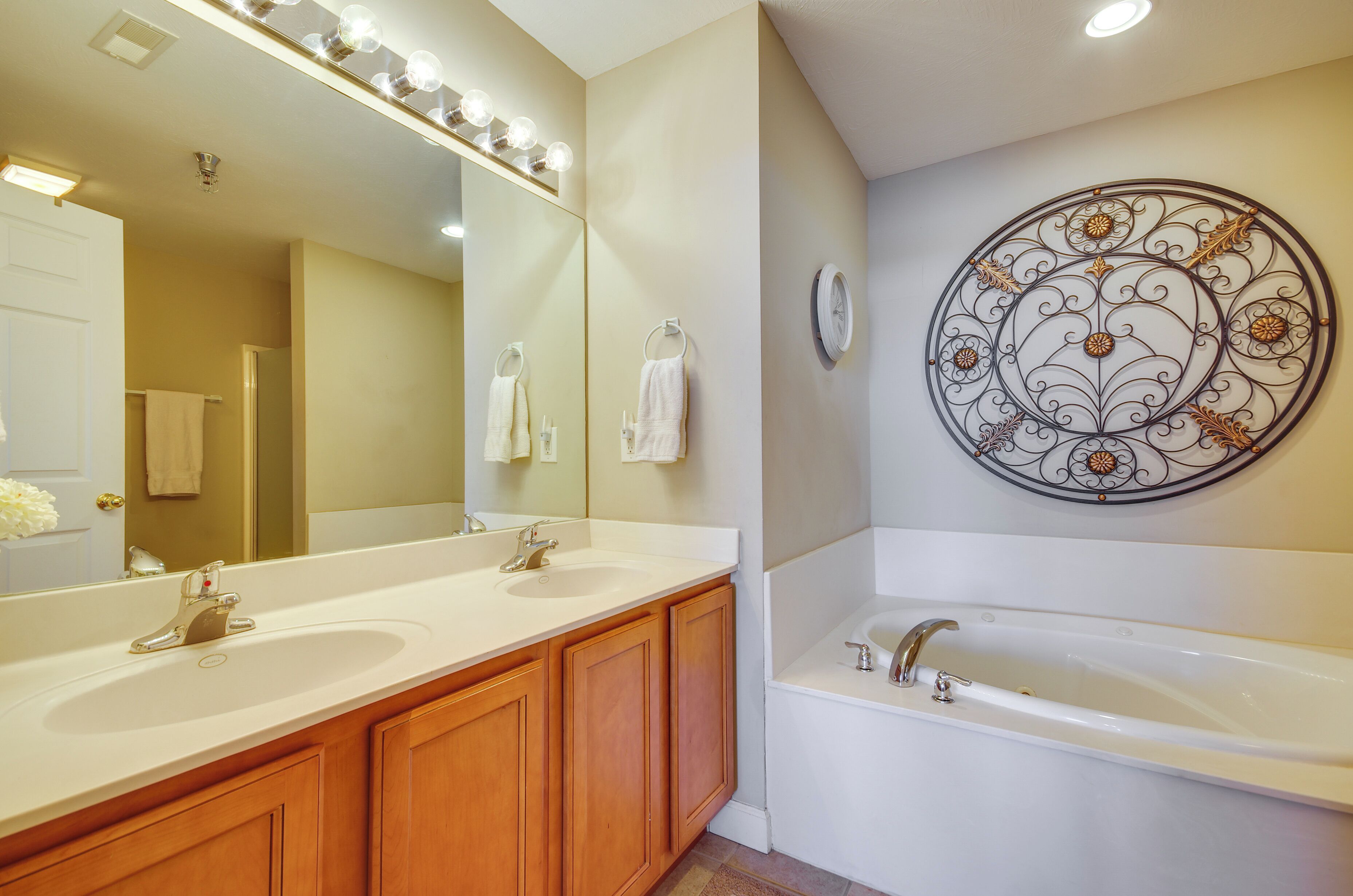 A bathroom with two sinks, a large mirror, a bathtub, and a decorative wall piece.