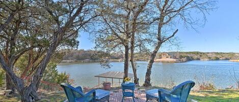 A patio with wicker chairs and a table overlooking a lake, with trees and a distant house visible.