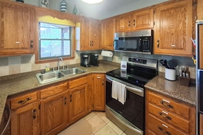 A kitchen with wooden cabinets, stainless steel appliances, a window, and a granite countertop. - Boat Dock! Lakefront Group Getaway in Eldon (Eldon)