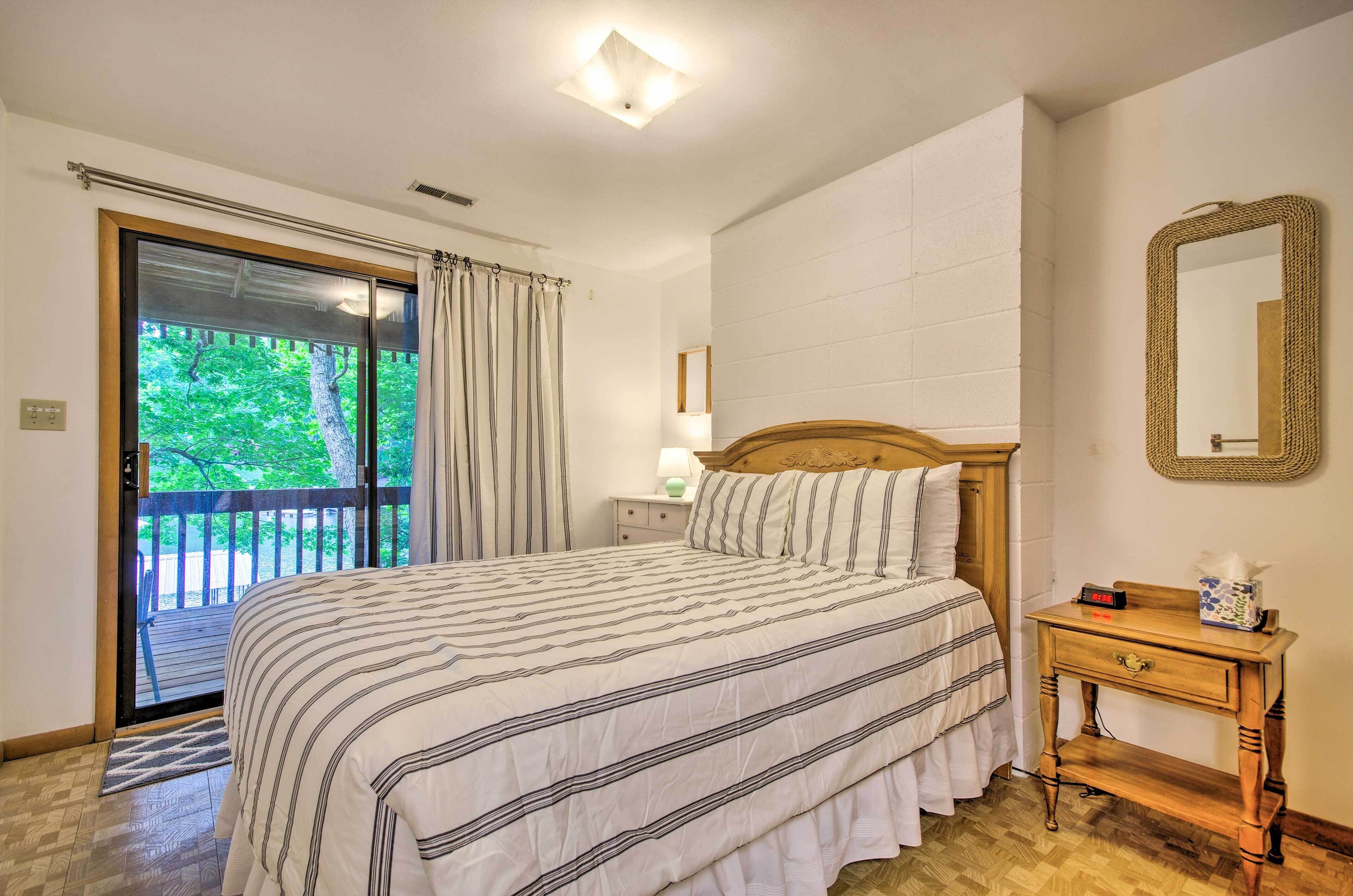 A bedroom with a large bed, a nightstand, a mirror, and a view of the outdoors through a sliding door.