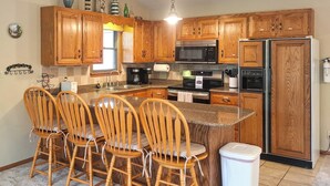A kitchen with wooden cabinets, a granite countertop, a stainless steel refrigerator, and a four-seat wooden bench. - Boat Dock! Lakefront Group Getaway in Eldon (Eldon)