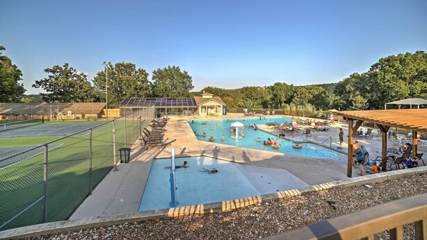 A swimming pool with a sunshade, a tennis court, and a small pavilion.