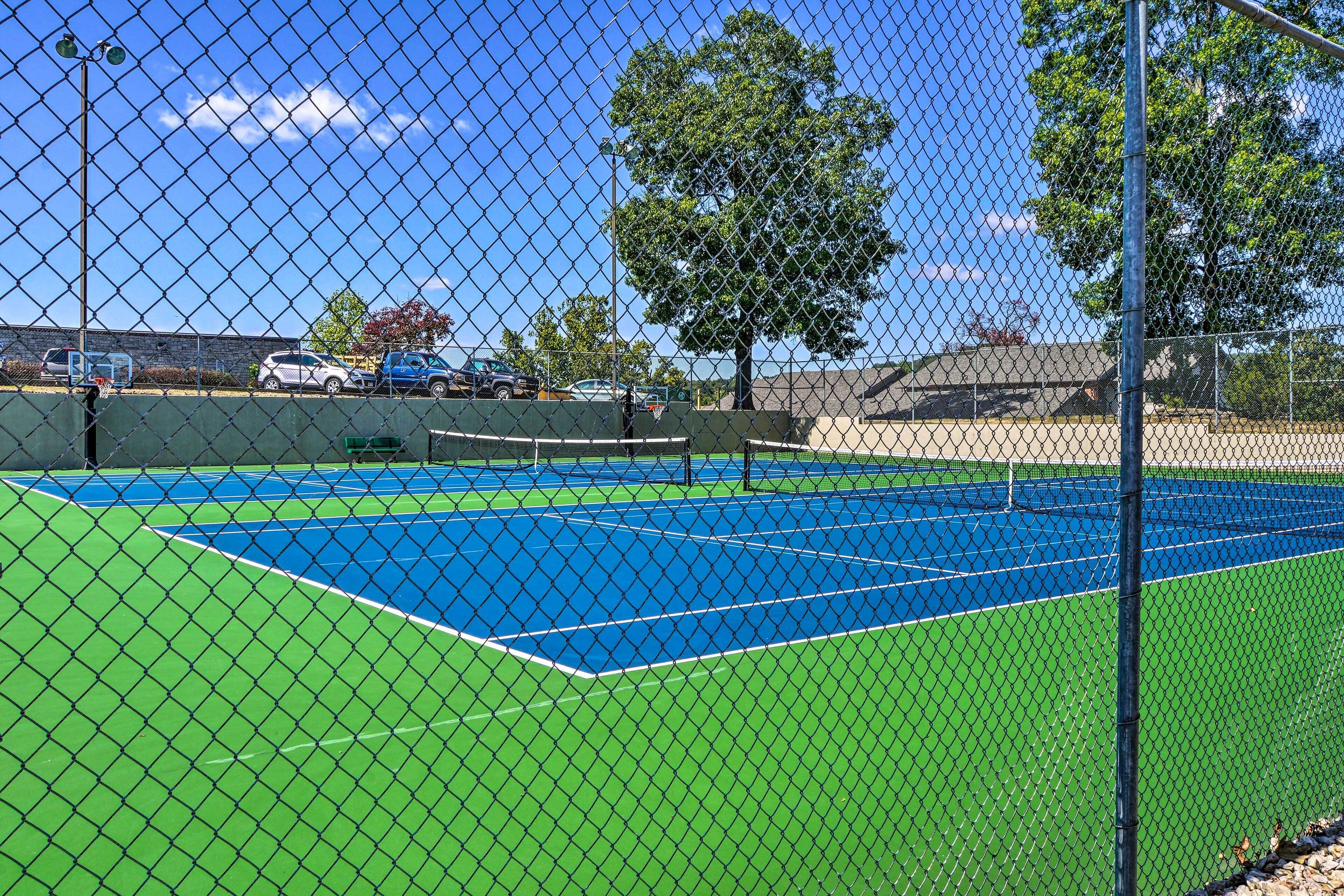 A tennis court enclosed by a chain-link fence with a clear blue sky and trees in the background.