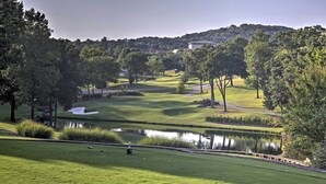 A golf course with a pond, trees, and a distant building.