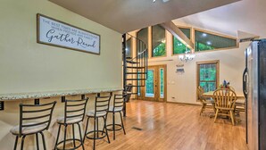 A kitchen with a bar area, wooden flooring, and a sign that says "The best times are always found when friends and family gather round." - Deck + Fire Pit: Lakefront Hideaway in Scranton! (Scranton)