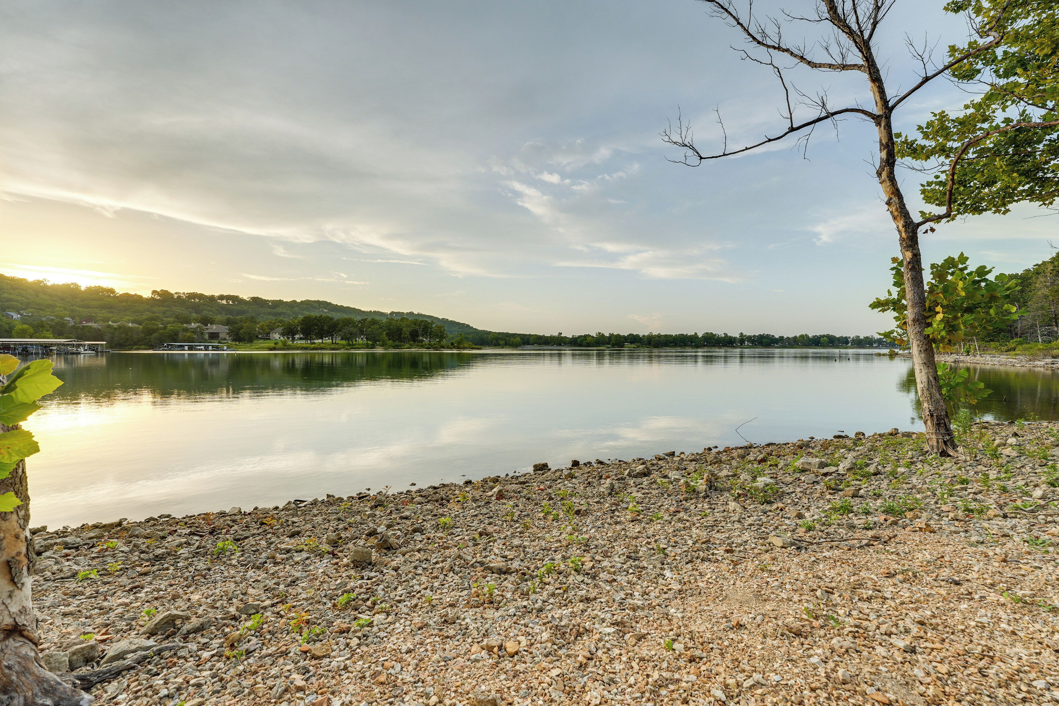 A calm lake with a rocky shoreline, surrounded by trees and hills.