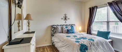 A bedroom with a bed, bedside table, lamp, ceiling fan, and a window with curtains.
