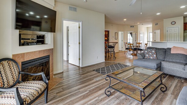 A spacious living room with a fireplace, a flat-screen TV, a ceiling fan, and a dining area in the background. - Lakefront Osage Beach Condo: Dock Your Boat Here! (Osage Beach)