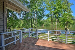 Eine Holzdielen-Terrasse mit weißen Geländern, die auf einen von Bäumen umgebenen See blickt.