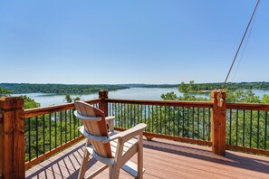 A wooden deck with a chair overlooking a lake and forest. - Luxe Table Rock Lake Vacation Rental With Hot Tub! (Lampe)