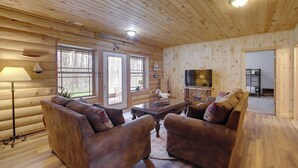 L’intérieur d’une cabane en rondins, avec un plancher en bois, un ensemble de meubles de salon, un téléviseur et une cheminée.