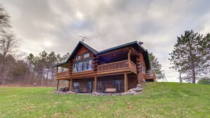 Une cabane en rondins dotée d’un balcon, d’une véranda et offrant une vue sur la forêt environnante.