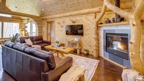 L’intérieur chaleureux d’un chalet en rondins, avec un canapé en cuir, une table basse en bois, une cheminée et un téléviseur fixé au mur.