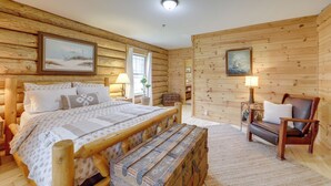 Une chambre dans une cabane en bois, avec un lit, un banc, une chaise et deux tableaux accrochés aux murs.