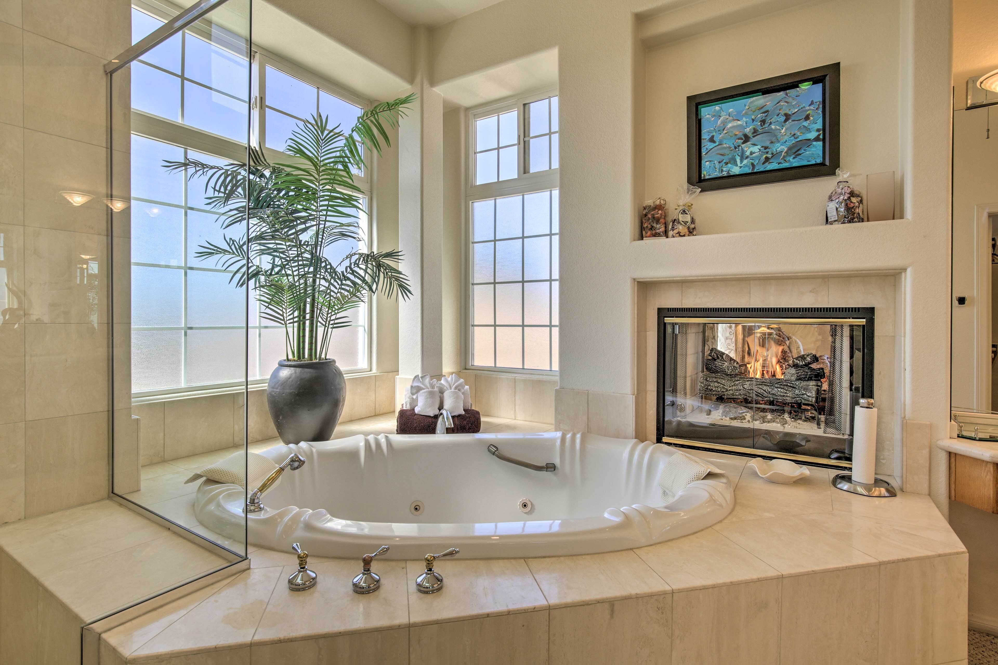 A spacious bathroom with a large bathtub, a glass shower enclosure, a fireplace, and a large window providing natural light.