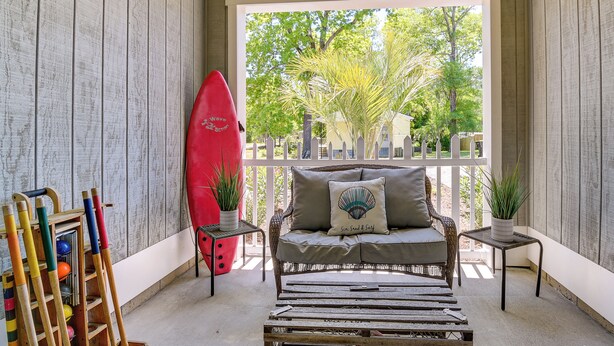 Un espace patio accueillant avec un canapé en osier, une planche de surf rouge et une table en bois.