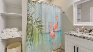 Une salle de bain avec un rideau de douche orné d’un motif de flamant rose, un lavabo avec un plan de travail en marbre et un miroir au-dessus du lavabo.
