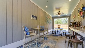 Une pièce aux murs lambrissés, dotée d’un ventilateur de plafond, d’un coin cuisine avec des tabourets et d’une table à manger avec des chaises.